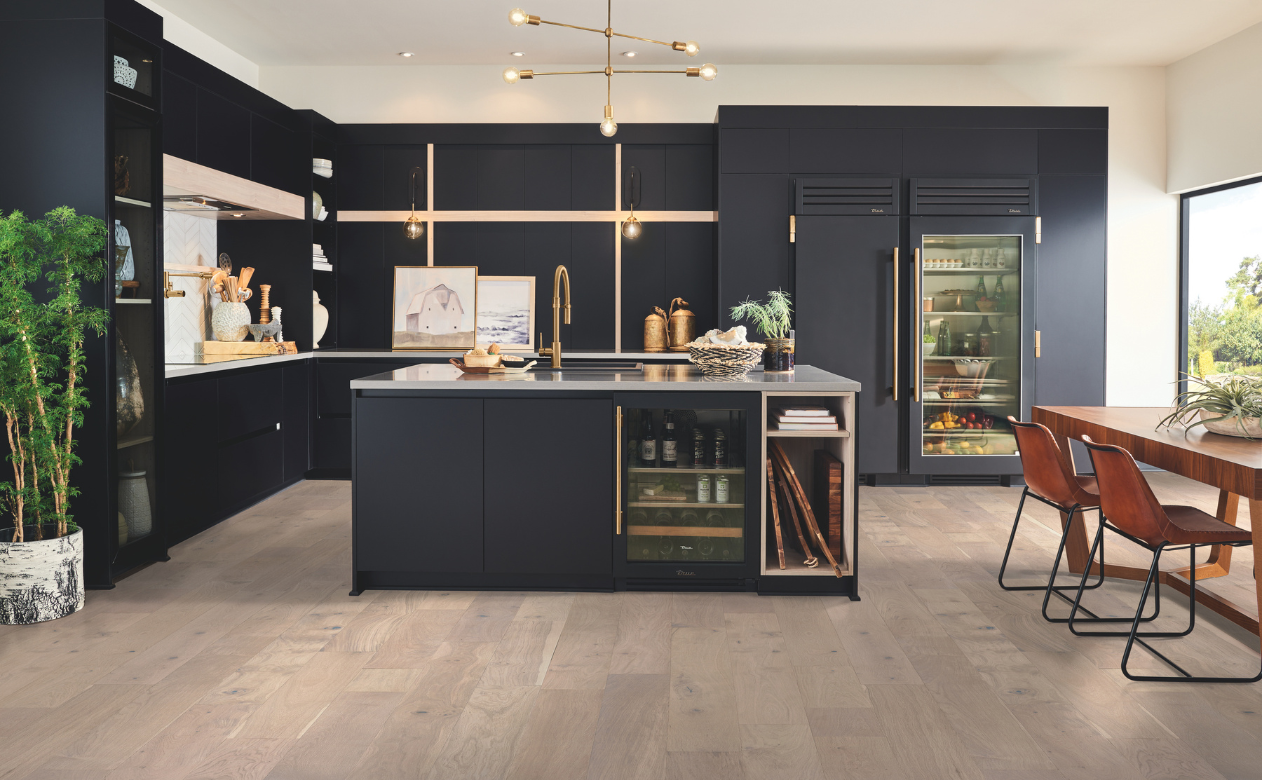 Hardwood flooring in a kitchen with dark cabinetry and gold accents